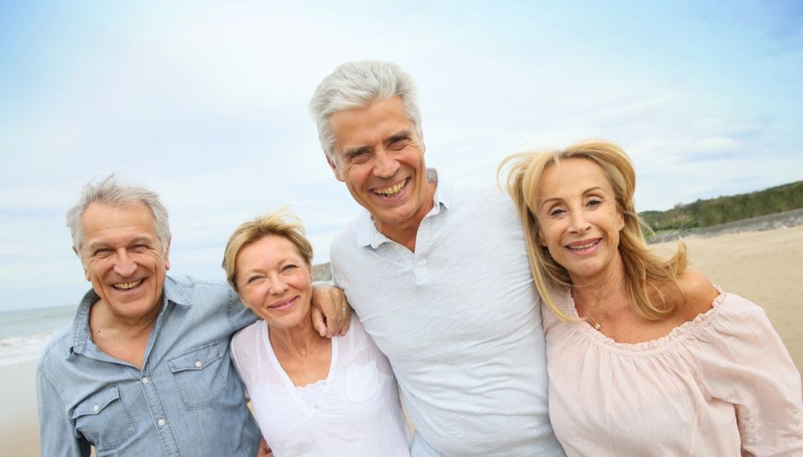 Two couples of seniors higging and smiling in front of beach