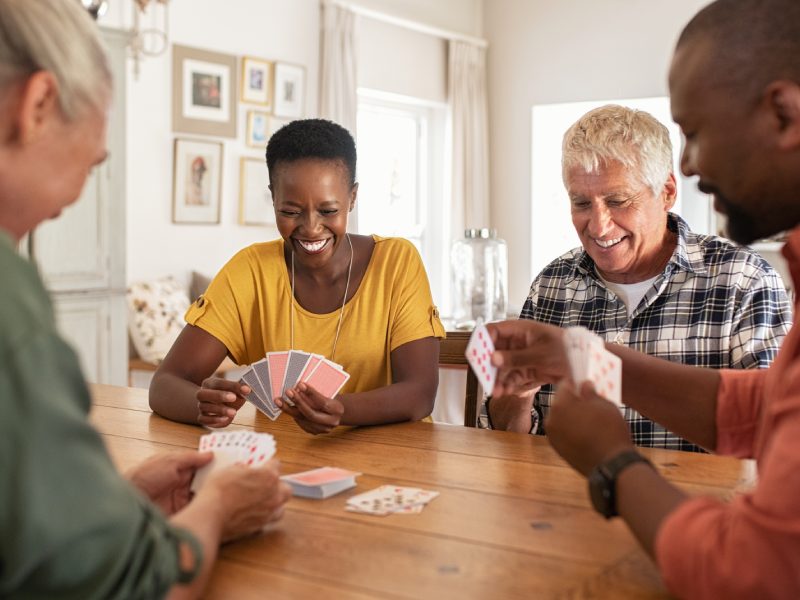 Retired multiethnic people playing cards together at home. Happy senior friends with african couple playing cards. Cheerful active seniors playing game at lunch table.