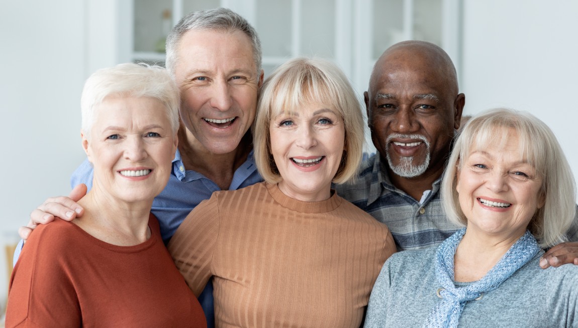 Portrait of multiracial group of happy senior friends men and women in casual outfits enjoying time together, cheerfully smiling at camera, kitchen interior. Elderly people lifestyle