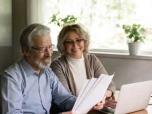Excited elder family pensioner couple read and check financial document, calculate profit, saving income from investment. OAP Senior man and 50s woman do monthly paperwork, make utility payment online