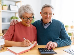 Elderly married couple sitting at the desk with a paper receipt in hands are calculating expenses, managing the family budget.
